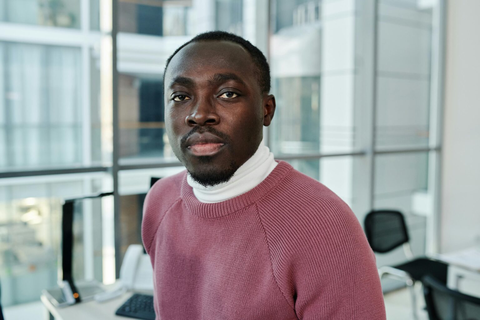 Portrait of a confident man in a cozy sweater in a bright, modern office environment.